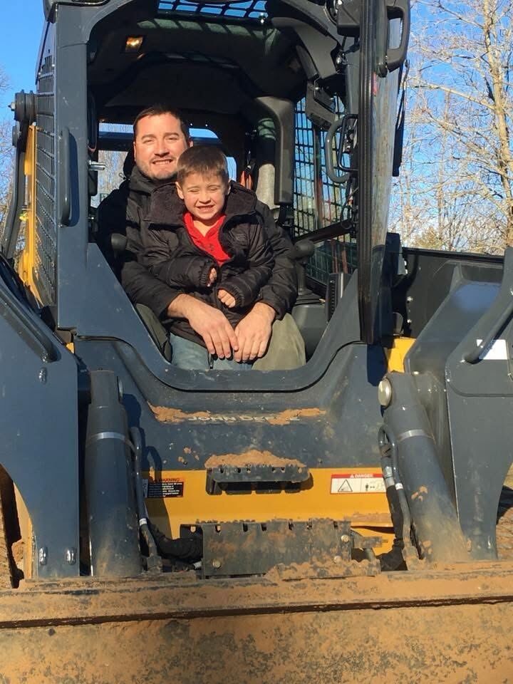 Josh Walker and his son together in the cab of a skid steer, both smiling