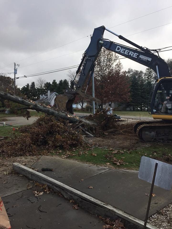 Excavator removing storm-damaged tree debris from a residential yard